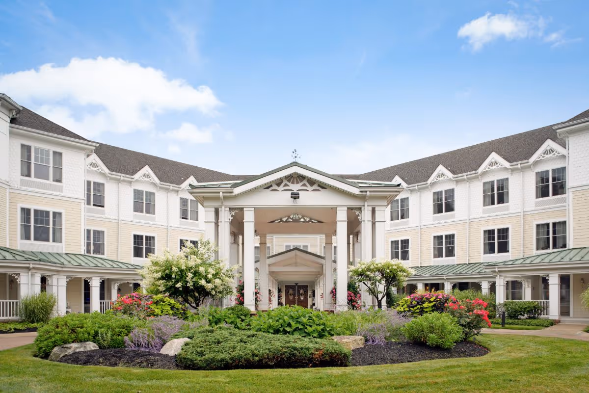Front entrance of a multi-story senior living building with a covered portico and landscaped circular garden.
