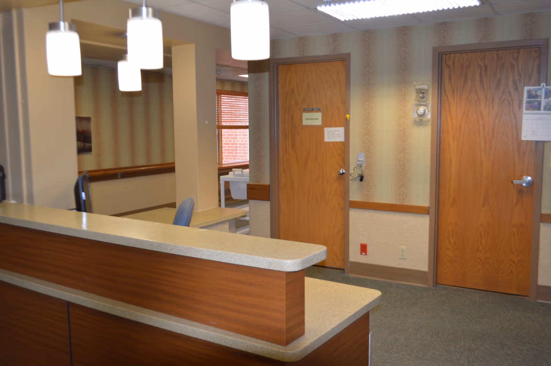 Reception desk and hallway inside a senior living facility with pendant lights and two wooden doors.