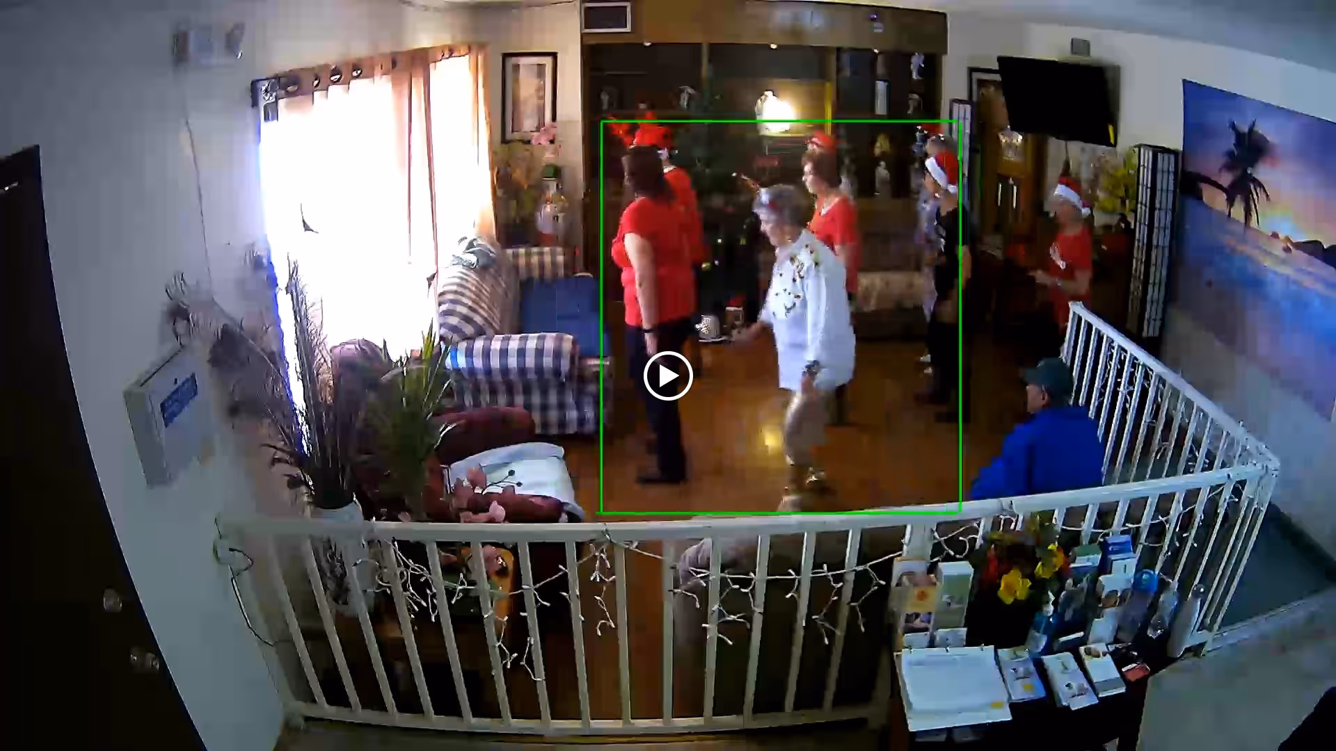 Several people in holiday attire dancing in a communal living room with couches and a white railing in the foreground.