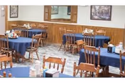 Communal dining room with round tables covered in blue tablecloths, wooden chairs, and place settings.
