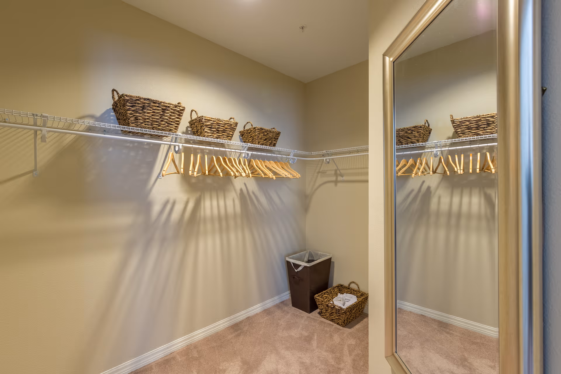 Walk-in closet with wire shelving holding wooden hangers and wicker baskets, a mirror on the door, and a laundry hamper.