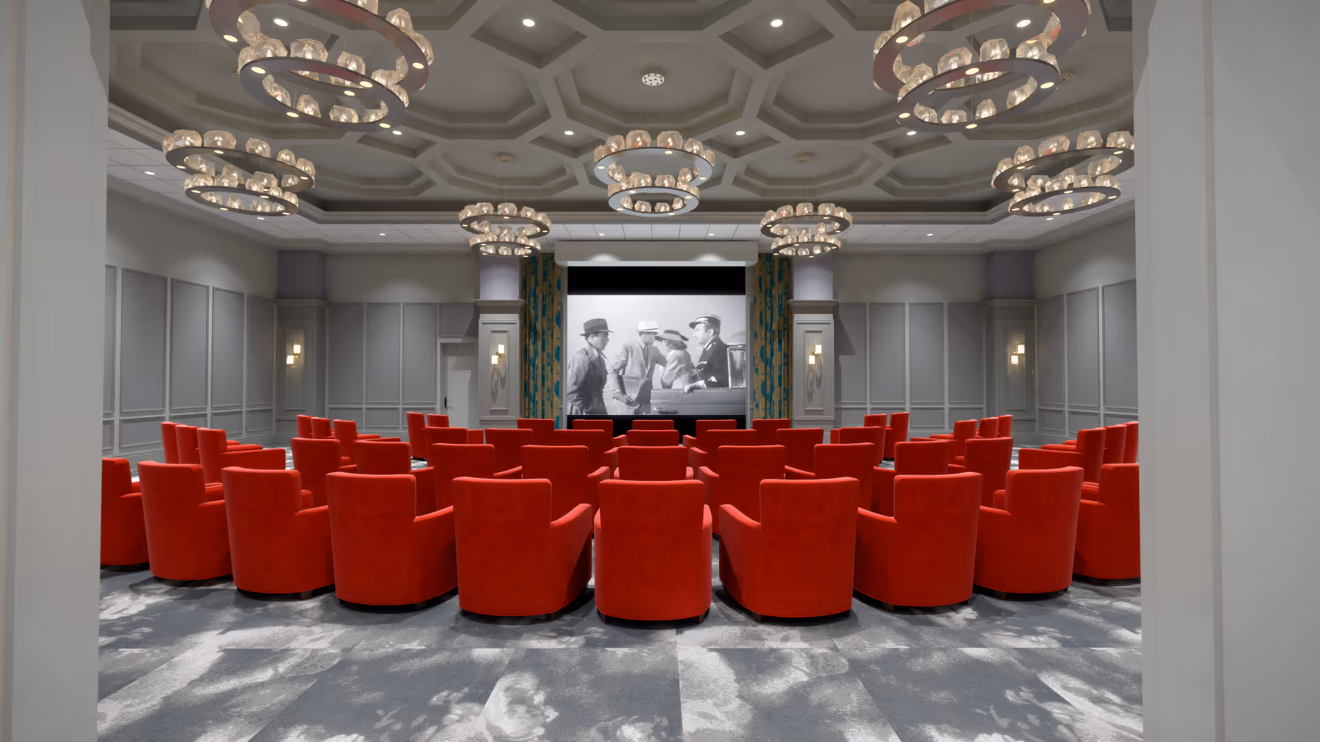 Screening room with rows of red armchairs facing a projection screen in an ornate interior auditorium.