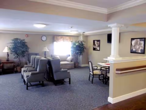 Senior living lounge with blue chairs, lamps, plants, and framed wall art.