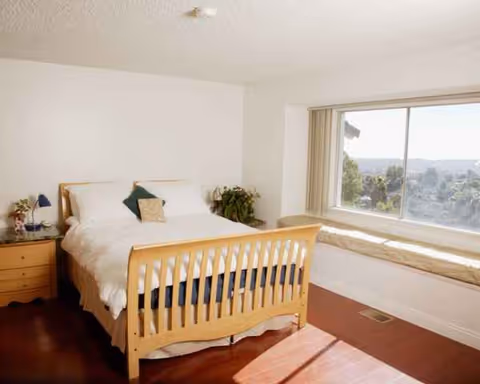 A wooden bed with white bedding faces a bright window seat in a bedroom.