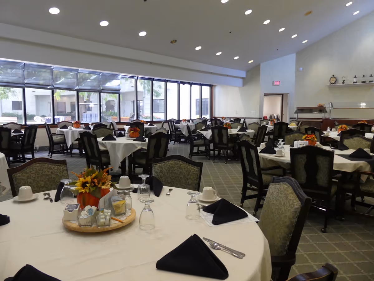 Spacious dining room with multiple round tables set with white tablecloths, black napkins, glassware and floral centerpieces.