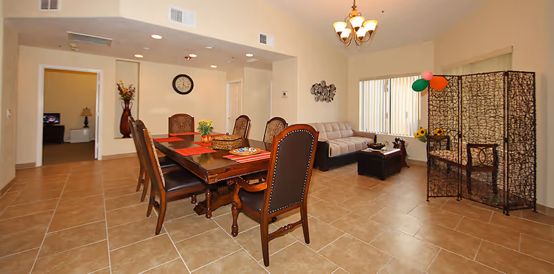Spacious assisted living common area with a dining table, chairs, sofa, and decorative divider.