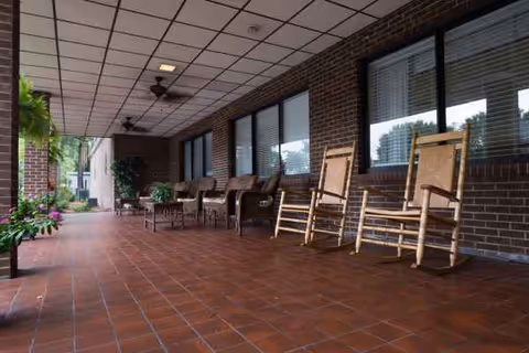 Covered outdoor patio with brick floor, rocking chairs, and potted plants.