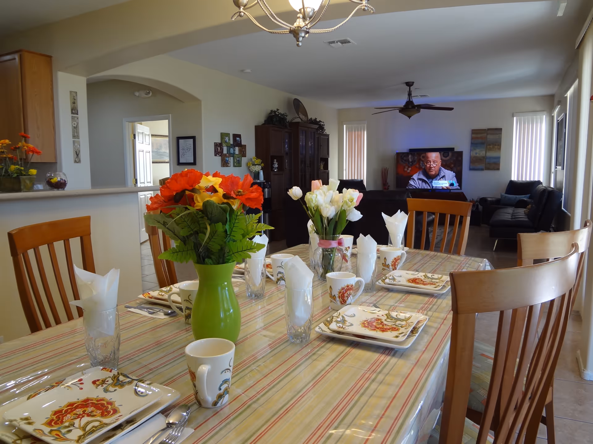 A dining table set with floral dishes and vases of flowers in an open-plan dining and living area with a TV visible in the background.