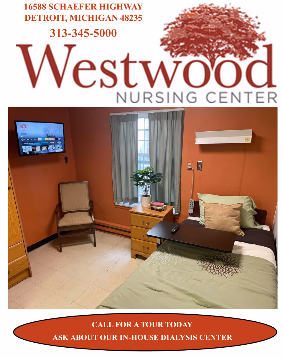 A small nursing center bedroom with an orange wall, a single bed with green and beige bedding, a wooden overbed table, a wooden nightstand with a potted plant and books, a beige cushioned chair, a window with gray curtains, and a wall-mounted TV displaying a streaming service interface.