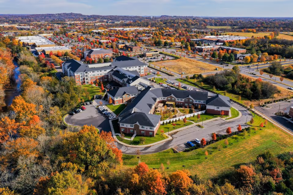 Aerial view of Clarendale at Indian Lake senior living facility surrounded by autumn trees with colorful foliage, parking lots, and nearby buildings under a clear sky.