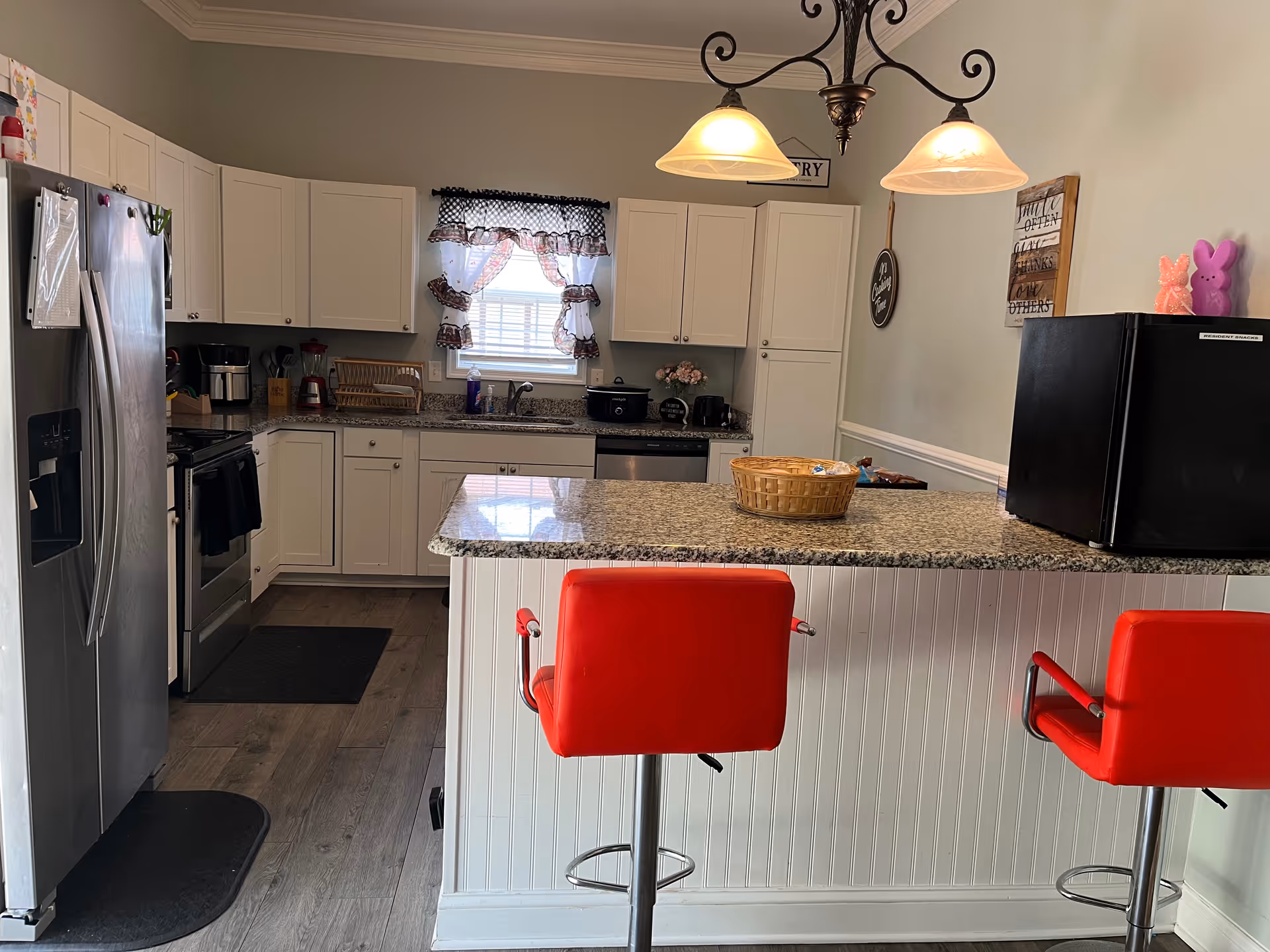 Bright kitchen with white cabinets, a granite-topped island and two red barstools.