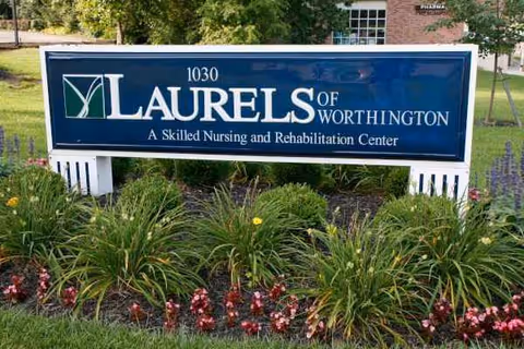 Blue Laurels of Worthington sign with greenery and flowers in front