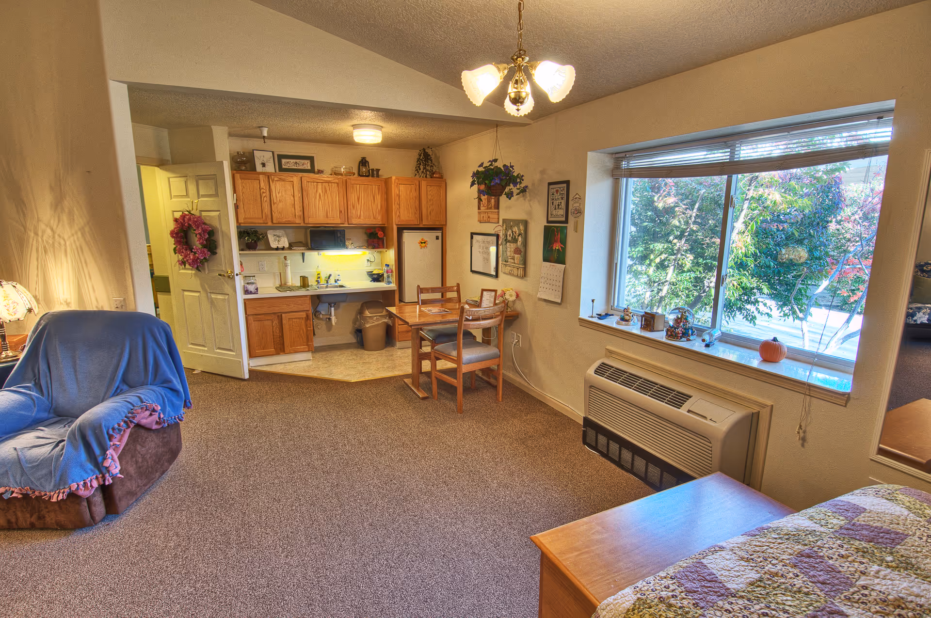 Bright studio apartment interior with a kitchenette, small dining table, armchair, large window and bed.
