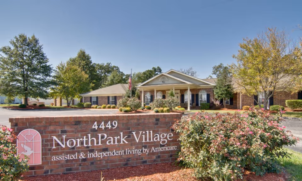 Brick entrance sign for NorthPark Village in front of the single-story senior living building and landscaped grounds.
