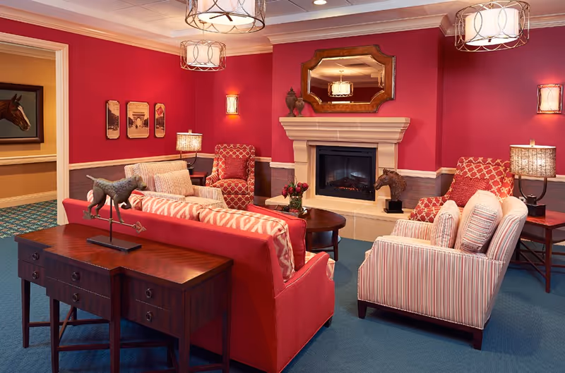 Cozy communal living room with red walls, a fireplace, and upholstered sofas and armchairs arranged around a coffee table.