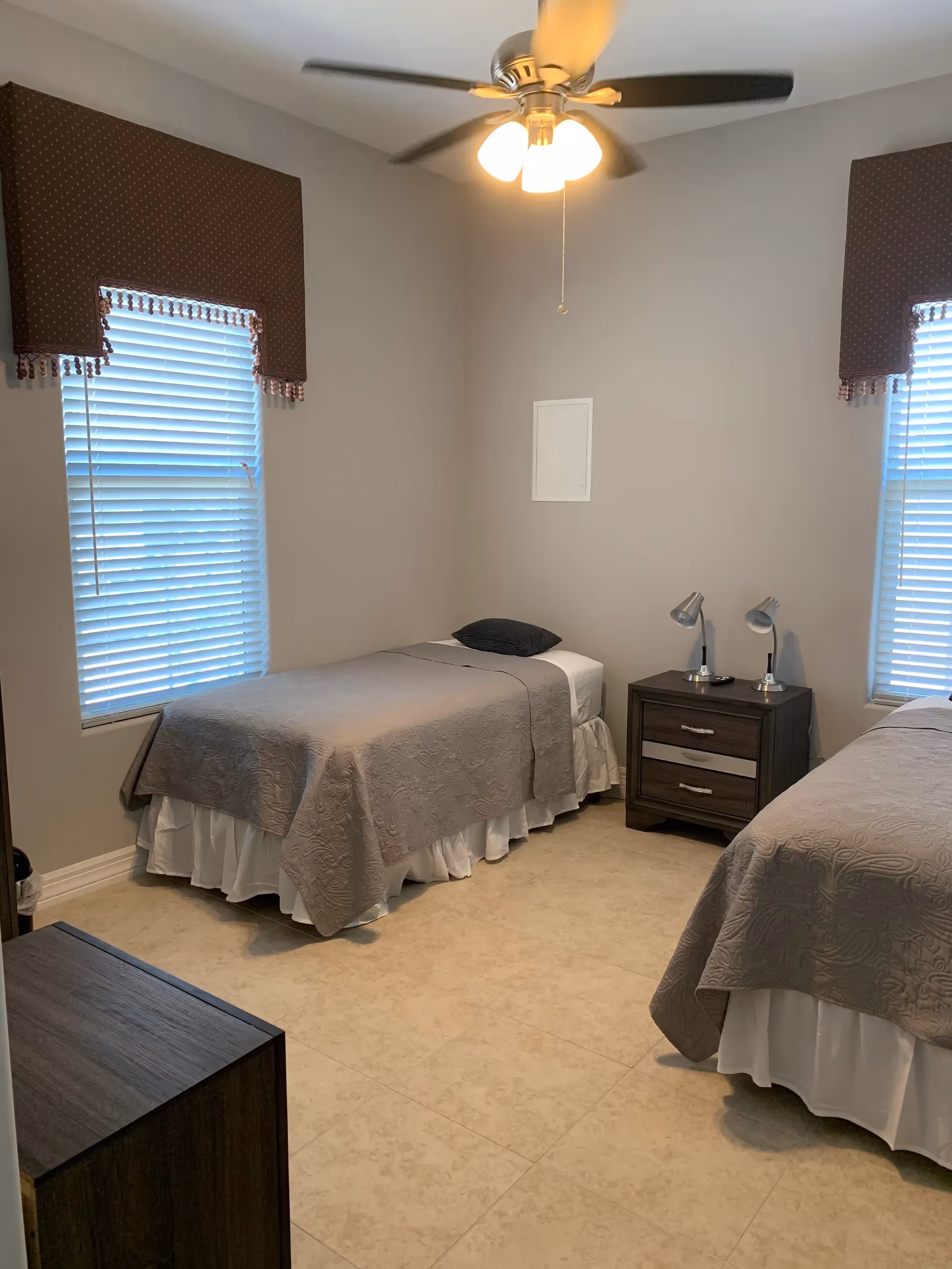 Two twin beds share a bedroom with nightstand, lamps, ceiling fan, and windows.