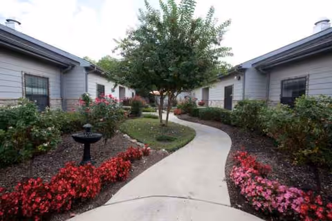 A curved concrete walkway winds between single-story buildings, bordered by colorful flower beds.