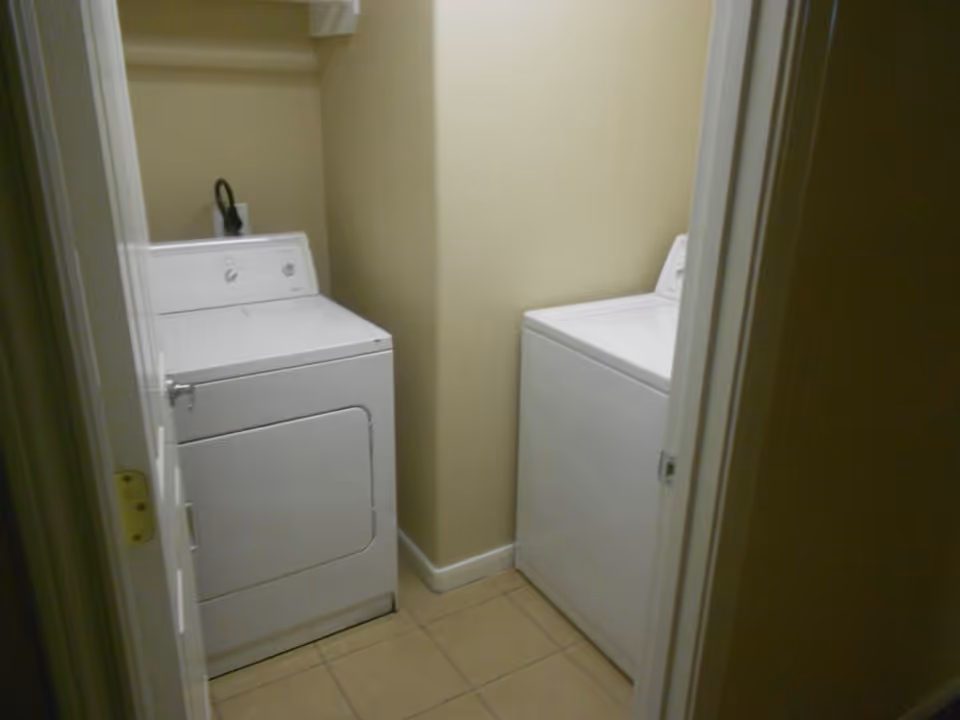 Narrow laundry room with a white front-loading dryer and a white top-loading washing machine on a tiled floor.