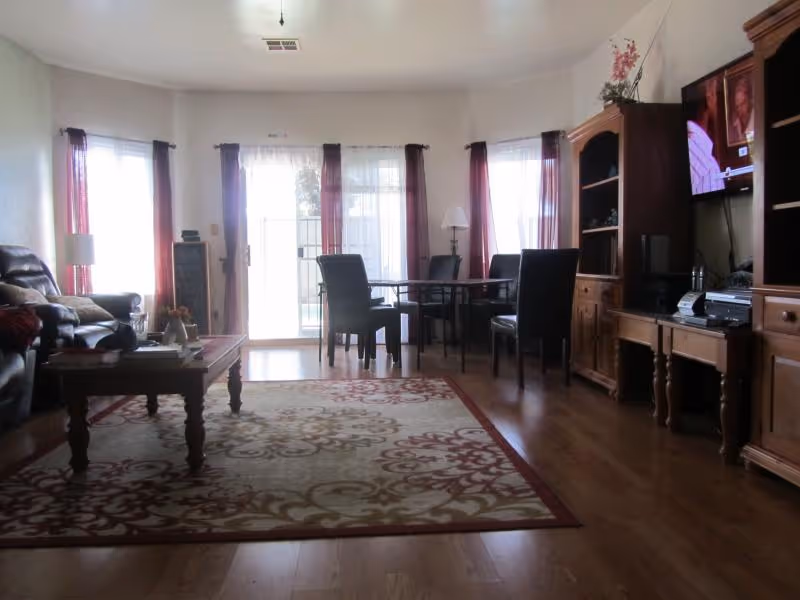 Spacious living room with seating, a patterned area rug, dining table by sliding glass doors, and wooden entertainment cabinets with a TV.