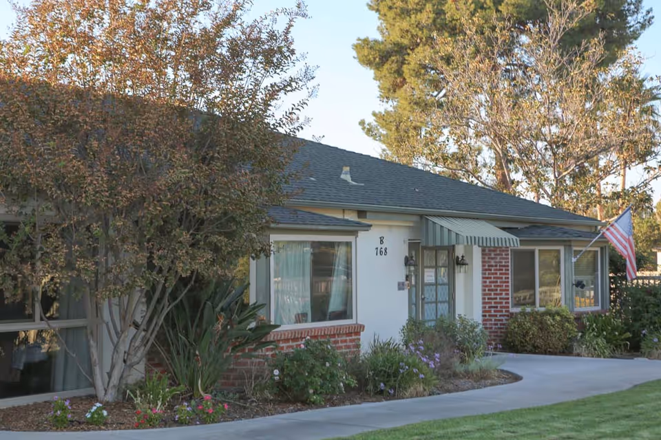 Single-story building entrance with brick facade, windows, awning, landscaped beds and an American flag.