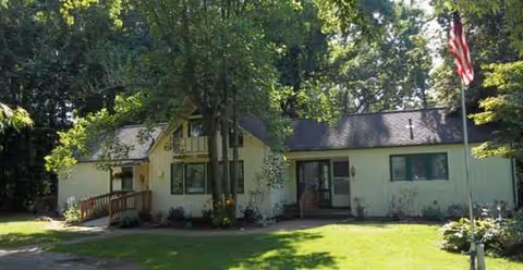 A small, single-story facility with beige exterior, green shutters, a flag, and a front yard.
