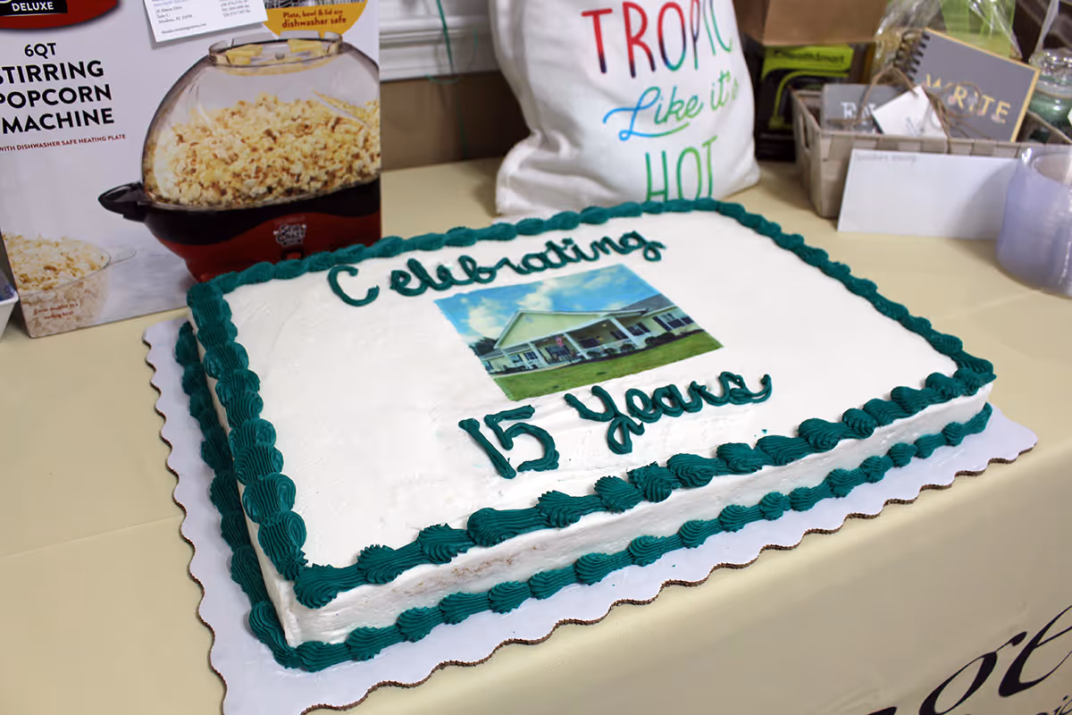 Rectangular celebration cake with green icing that reads "Celebrating 15 Years" and a photo of a building on top, set on a table.