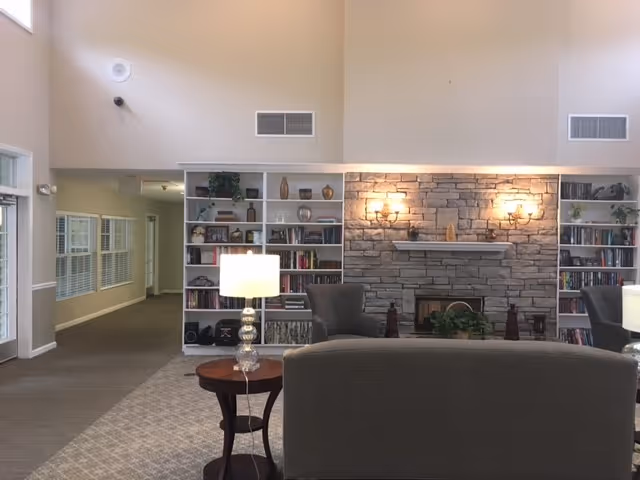 Communal living room with sofas facing a stone fireplace flanked by built-in bookshelves and table lamps.