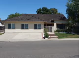 Single-story beige senior living facility front with driveway, small porch, and lawn