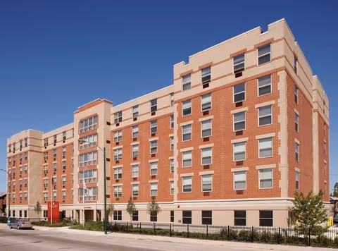 Brick, multi-story senior living facility along a street with a clear blue sky.