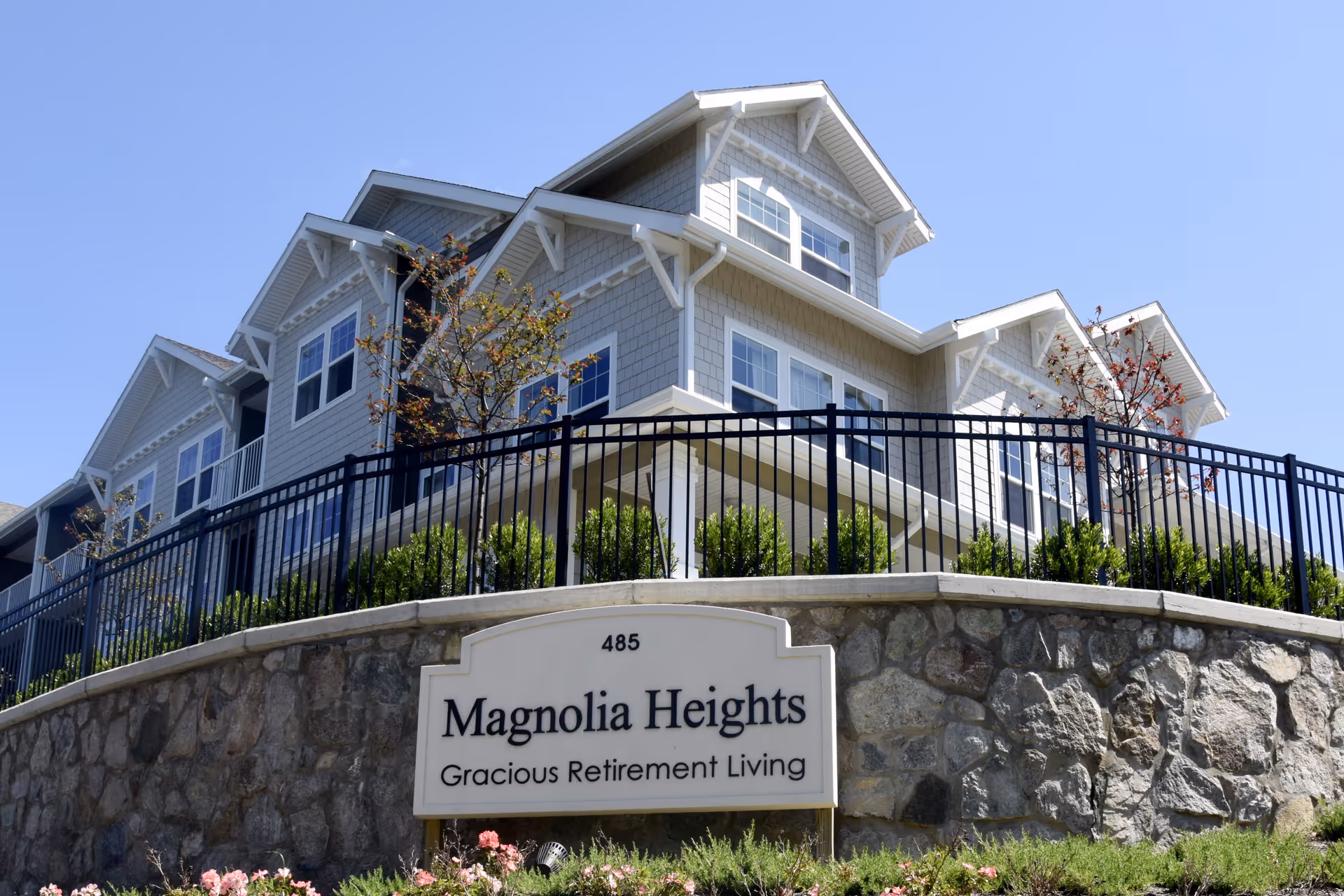 Exterior view of a multi-story residential building behind a stone wall and sign reading "Magnolia Heights Gracious Retirement Living."