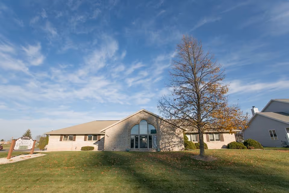 Front view of the Scandinavian Court Assisted Living brick building with a tree on the lawn under a blue sky.
