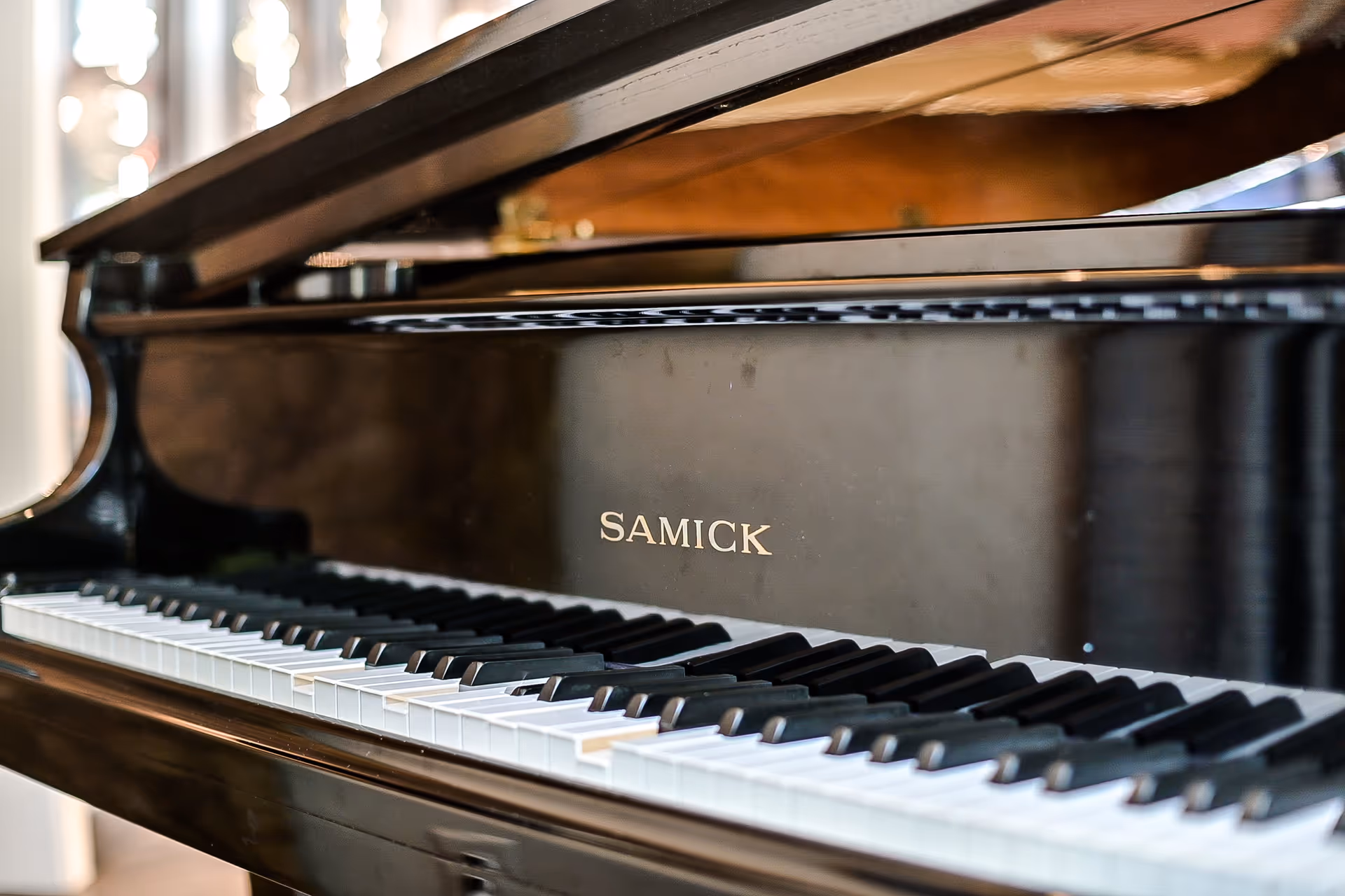 Close-up view of a black Samick grand piano keyboard with the lid partially open, showing the piano keys and the brand name on the side.