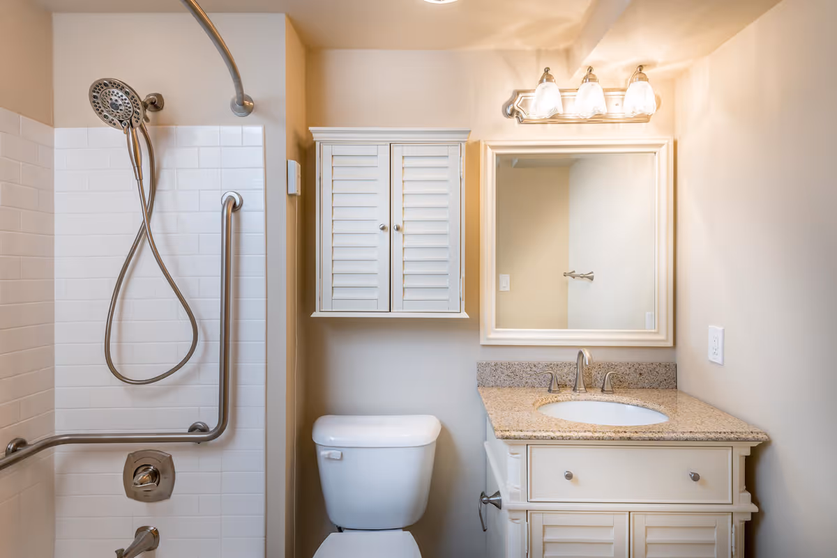 Well-lit bathroom with a walk-in shower, toilet, vanity with sink and mirror, and a wall-mounted cabinet.