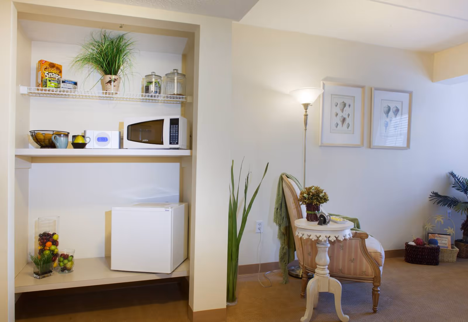 Small living area with a kitchenette nook containing a microwave and mini-fridge, and a chair with a side table and floor lamp.