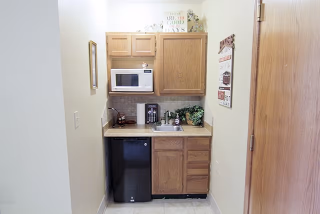 Small kitchenette alcove with wooden cabinets, a microwave, mini fridge, sink, and countertop appliances.
