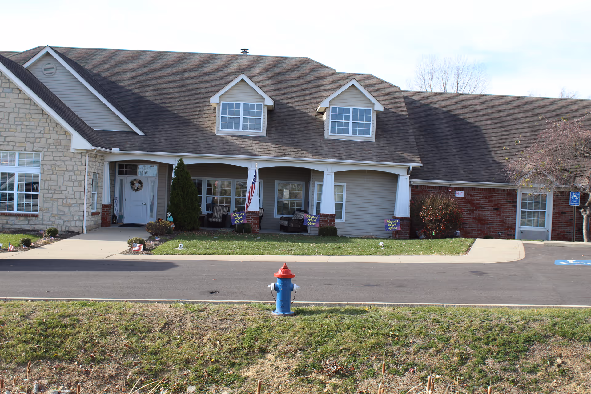 Front view of a senior living building with a covered porch, American flag, seating, and a fire hydrant in the foreground.
