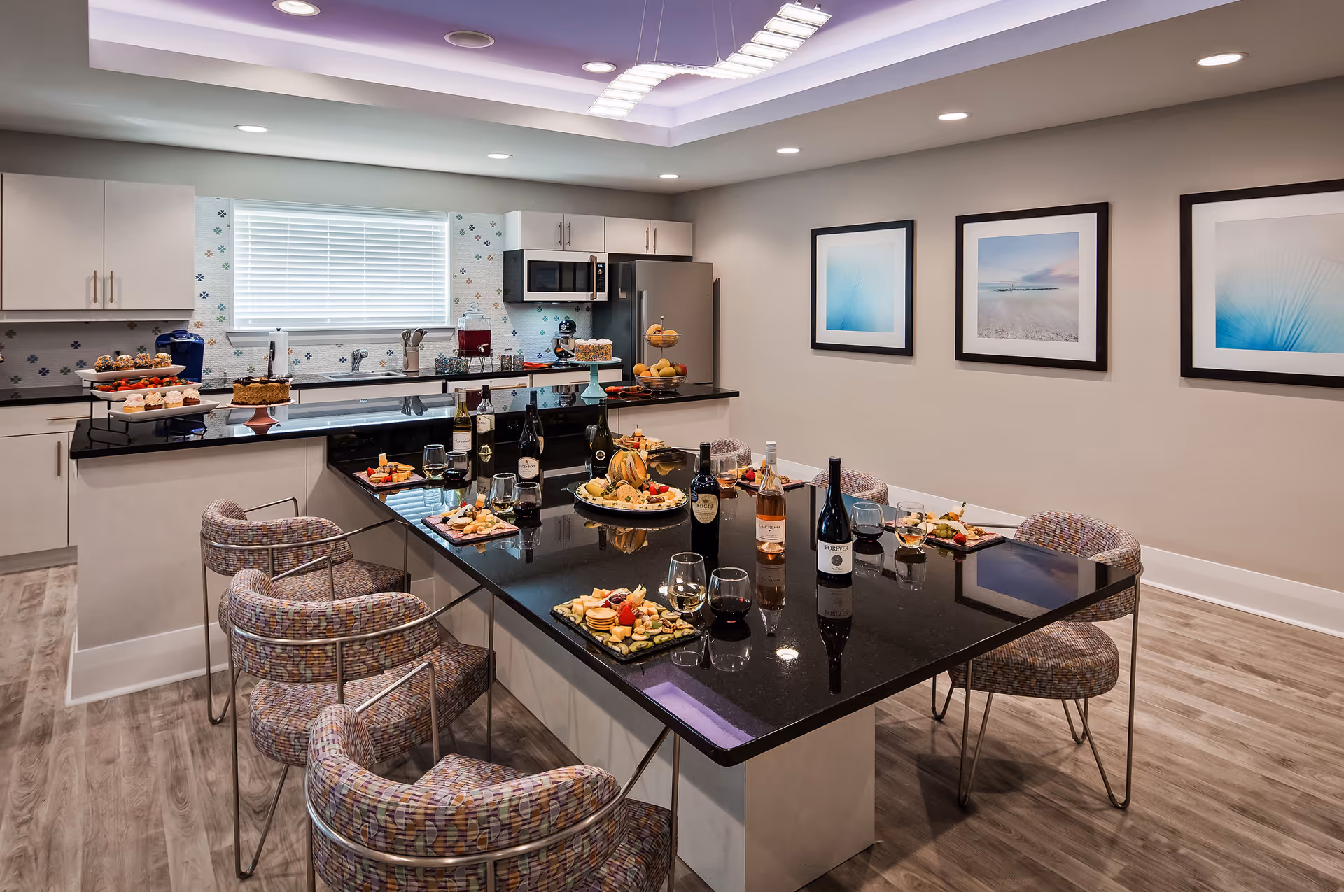 Modern communal kitchen and dining area with a large black island set with wine, glasses, and appetizers and surrounded by patterned chairs.