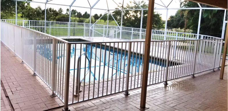 A fenced, screened-in outdoor swimming pool with a brick patio and white metal railing.