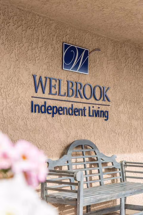 Exterior wall of Welbrook Independent Living with a blue bench and signage.