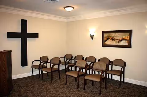 A small beige-walled room with brown chairs arranged in rows, cross wall art, and a podium.