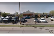 Single-story brick senior living building with a covered entrance and a parking lot with several cars in front.