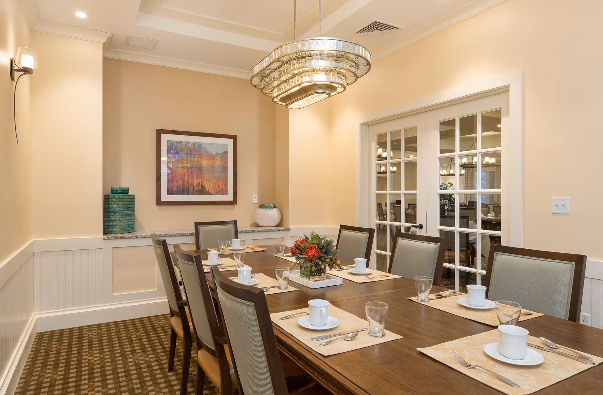 Elegant dining room with a long set table, chandelier, framed artwork, and glass-paneled double doors.