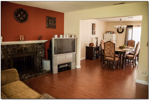 Open living area in a senior care home with fireplace, TV, and adjacent dining table.