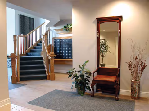 Lobby area with a carpeted staircase, a wall of mailboxes, a tall mirror with a wooden bench, and potted plants.