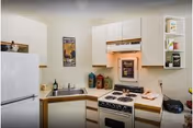 Compact white kitchen with cabinets, refrigerator, sink, stove and various countertop items.