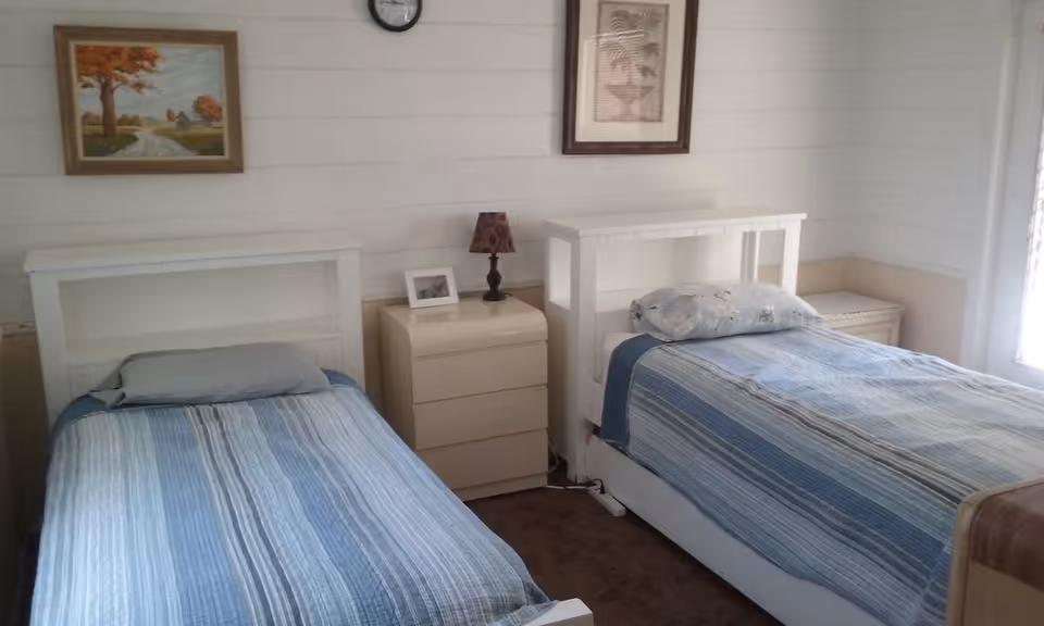 Two twin beds with blue striped bedspreads, a shared nightstand with a lamp, and framed artwork on white paneled walls.
