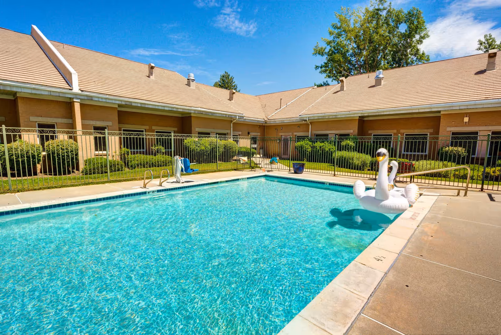 Outdoor swimming pool with a white swan float in front of a single-story brick building under a blue sky.