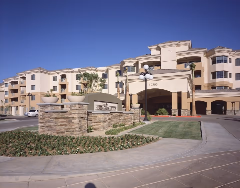 Exterior front entrance of The Heritage Tradition senior living building with a stone sign and covered porte-cochère.