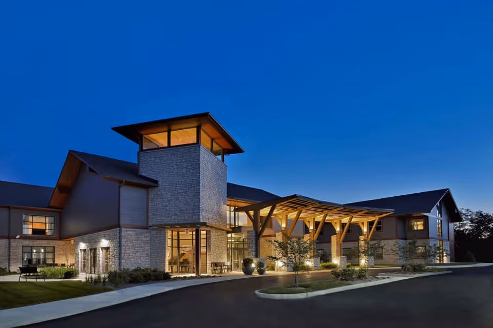 Exterior view of Wellbrooke of Westfield building at dusk with illuminated entrance, stone and wood architectural features, and a clear blue sky.