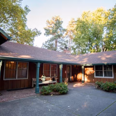 One-story wooden facility with a courtyard, bench, and surrounding trees.